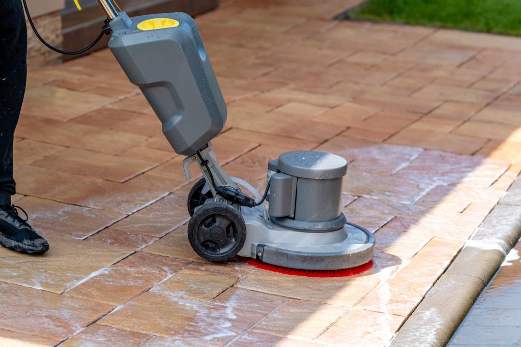 chemical machine cleaning concrete pavement in front of the house with a brush
