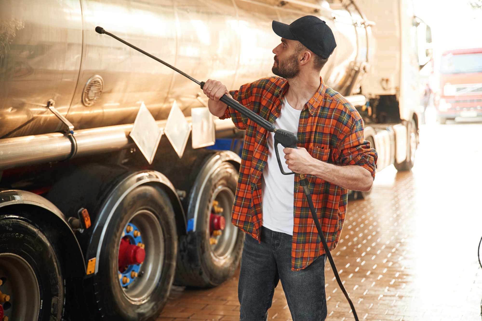 Fuel tanker is getting washing. Young truck driver in casual clothes