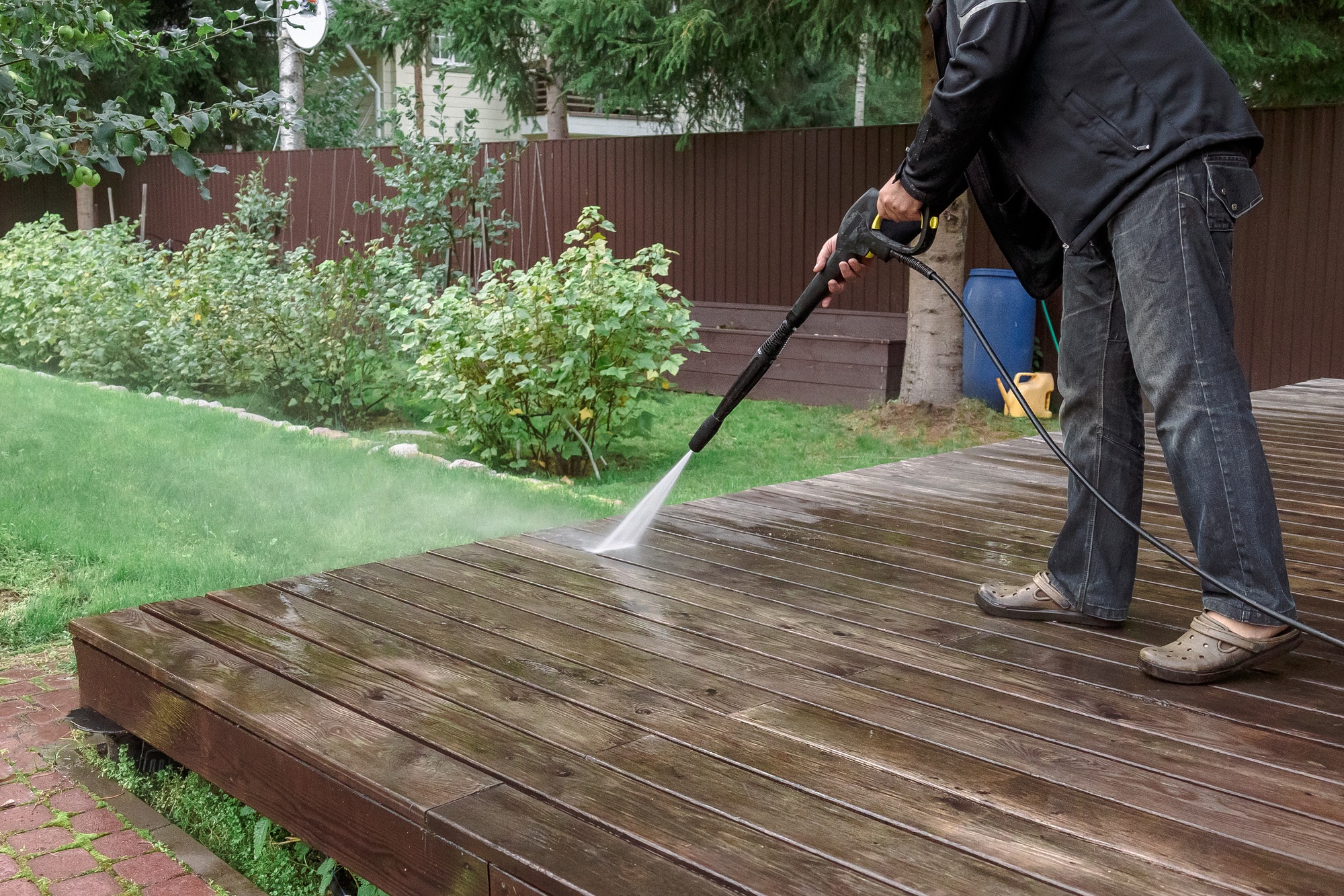 Man cleaning walls and floor with high pressure power washer. Washing terrace wood planks and claddi